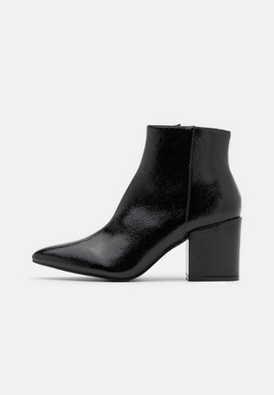Sort blank ankelstøvle med spids tå og blokhæl, glat tekstureret læder, lynlås i siden og minimalistisk design på hvid baggrund.