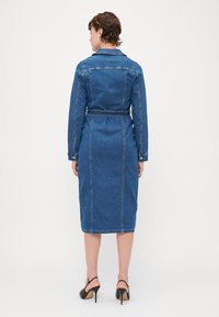 Jeans φόρεμα με μακριά μανίκια, μήκος μέχρι το γόνατο, εφαρμοστή μέση και ζώνη. Μπλε χρώμα με αντίθετο ραφές. Μαύρα ψηλοτάκουνα σανδάλια.