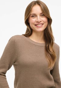 Maglione marrone a maglia con un motivo testurizzato, scollatura rotonda e maniche lunghe. Il tessuto ha un aspetto morbido e caldo.