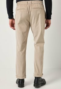 Pantaloni in corduroy beige con vita elasticizzata, due tasche posteriori e orli arrotolati, abbinati a calzature nere. Tessuto testurizzato visibile.