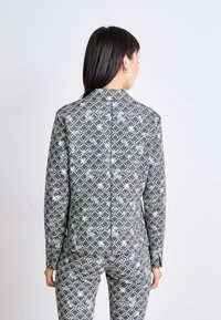 Gemusterter Anzug in Schwarz und Weiß mit hexagonalen und floralen Motiven. Lange Ärmel und eine taillierte Passform mit einem Rückennähten-Detail.