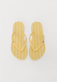 Tongs jaunes avec un motif de chaîne blanche. Semelle plate en caoutchouc et larges brides. Étiquette de marque sur le côté. Design léger et décontracté.