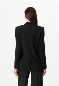 Blazer nero su misura con un design strutturato, rever affilati e un singolo spacco posteriore. Presenta polsini con bottone e una texture liscia.
