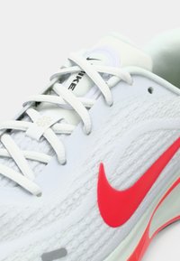 Αθλητικό παπούτσι Nike για τρέξιμο με επάνω μέρος από ανοιχτό γκρι ύφασμα, λευκά κορδόνια και φωτεινό κόκκινο λογότυπο Swoosh. Υφή με ανάγλυφο μοτίβο στα πλάγια.