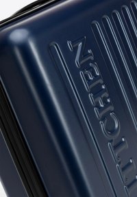 Námořnický tvrdý kufr s hladkým lesklým povrchem. Obsahuje vertikální rýhy a embosované logo pro přidanou texturu a detail.