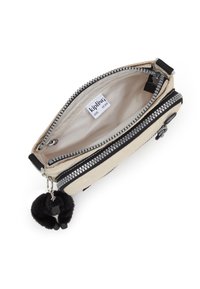 Kremowa saszetka zapinana na czarny zamek błyskawiczny z brelokiem w kształcie pompona. Wnętrze wyłożone jasną podszewką z metką Kipling.