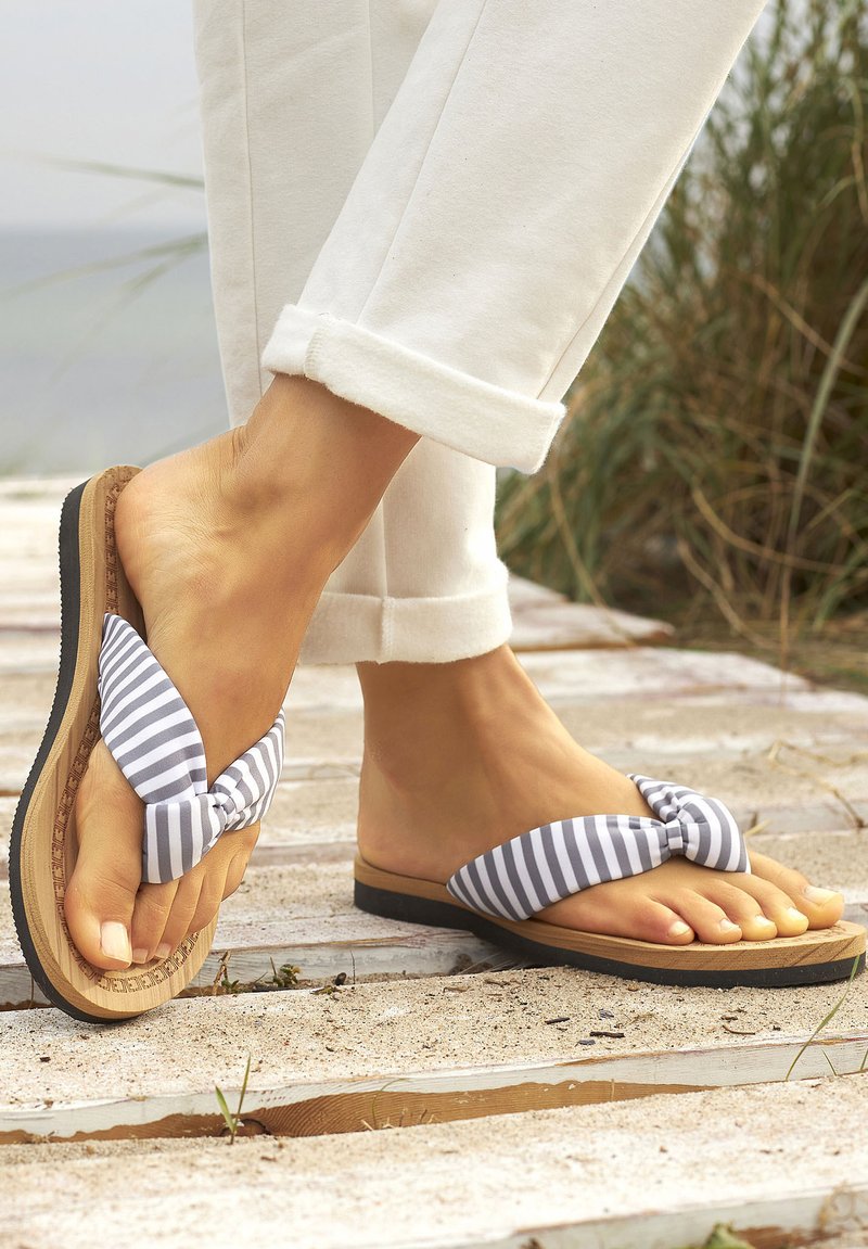 Gestreepte flip-flop sandaal met een geknoopte stof bovenkant, vlakke tan zool en een gestructureerde rubberen loopzool. G gedragen met opgerolde witte broeken.