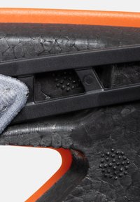 Sort tekstureret materiale med et reptilmønster, en orange accent og en grå remdetalje med små hævede prikker. Designet til greb og støtte.
