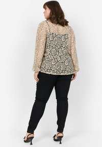 Sorte blondetop med lange ærmer, beige foring og blomsterprint. Sammen med sorte skinny jeans og højhælede sandaler. Bagfra.