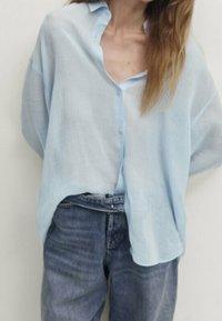 Ljusblå, knäppt skjorta gjord av ett genomskinligt tyg med en avslappnad passform, i kombination med högmidjade jeans i denim. Minimalistisk design med en mjuk textur.