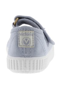 Scarpa in tela azzurra chiara con suola in gomma bianca, presenta un'asola e hardware dorato, e una patch con logo cucita sul retro.