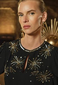 Vestido negro con bordado de estallido de estrellas metálicas doradas y plateadas, escote redondo con un recorte en forma de llave y mangas abullonadas.