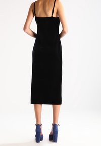 Musta samettinen midi-mekko, jossa on ohutolkaimet ja suora siluetti. Siinä on sileä pinta ja hienovarainen kiilto, yhdistettynä sinisiin korkokenkiin.