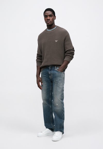 Γκρι υφασμάτινος πουλόβερ με ριγέ μανσέτες, συνδυασμένο με ανοιχτό μπλε τζιν παντελόνι. Λευκά sneakers ολοκληρώνουν το ντύσιμο.