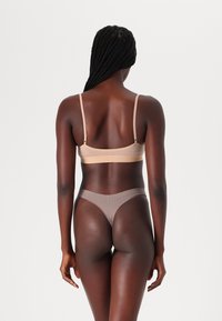 Bralette nude et string marron, confectionnés en tissu lisse. Le bralette présente des bretelles fines et un design sans couture. Le string possède une taille douce.