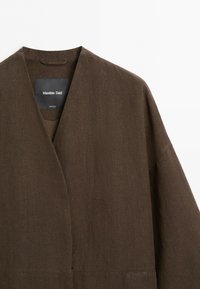Brown linen jacket with a V-neck collar and loose fit, showing the Massimo Dutti brand label inside the neckline.