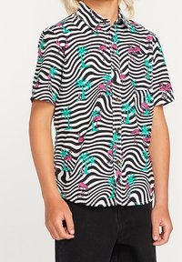 Chemise à manches courtes avec un motif de vagues noir et blanc, ornée de flamants roses et de palmiers verts, fabriquée en tissu léger.