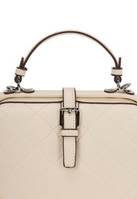 Cremefarvet quilted håndtaske med en struktureret form, der har et håndtag i toppen, sølvfarvet hardware og et brunt accentbælte med spænde detaljer.