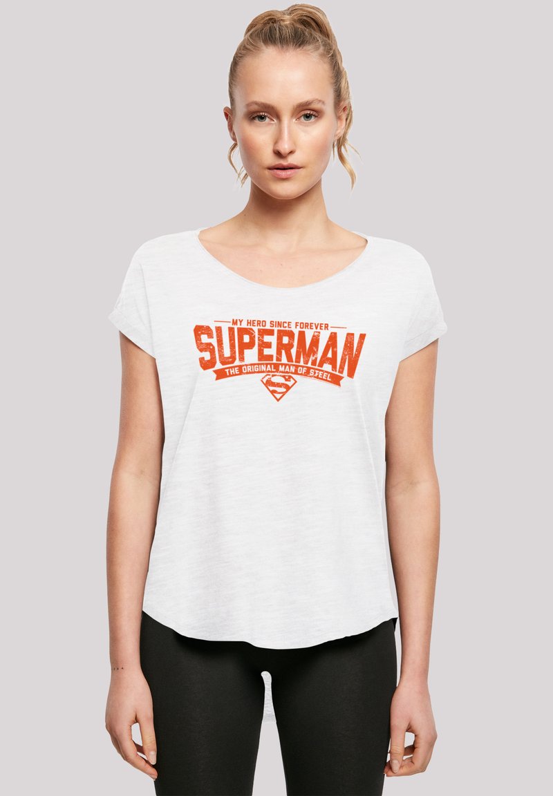 Bílá tričko s krátkým rukávem a kulatým výstřihem. Obsahuje oranžový grafický text "SUPERMAN" a další text nahoře a dole. Standardní střih.