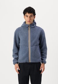 Fleece jacket in blue with a front zipper and hood. Features a soft texture, side pockets, and colorful stripes along the zipper.