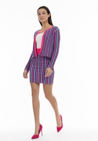 Cárdigan de punto a rayas en colores rosa, azul y lila, combinado con una falda ajustada a juego y tacones altos rosas. Textura suave en toda la prenda.