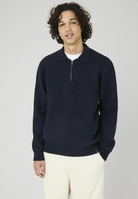 Pull en maille bleu marine avec un col zippé mi-hauteur, des poignets et un ourlet côtelés, offrant une texture douce et un design décontracté.