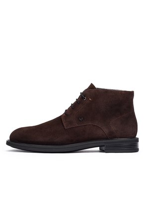 Bota de tobillo para hombre de ante marrón oscuro con cordones negros y suela baja de goma negra, vista lateral sobre fondo blanco.