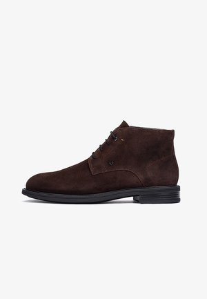 Dunkelbraune Wildleder-Herren-Stiefelette mit schwarzen Schnürsenkeln und niedriger schwarzer Gummisohle, Seitenansicht auf weißem Hintergrund.