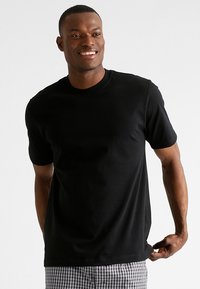 Zwarte korte mouw t-shirt gemaakt van katoen met een ronde halslijn, soepel aansluitend, gedragen met geruite shorts. Textuur van de stof zichtbaar.