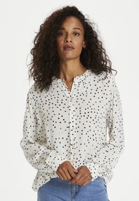 Vit långärmad blus med knäppning fram, med ett spritt prickmönster i svart, brunt och rosa. Mjuk texturerad tyg.