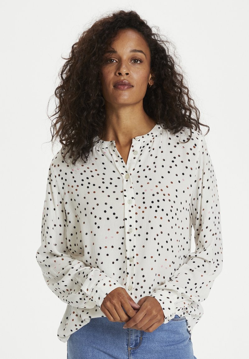 White long-sleeve blouse with a buttoned front, featuring a scattered polka dot pattern in black, brown, and pink. Soft textured fabric.