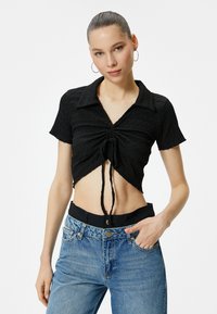 Sort cropped bluse med struktureret stof, korte ærmer og bindebånd foran. Matchet med lyseblå højtaljede jeans.