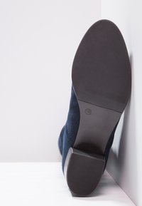 Navy suede ankle boot with a textured rubber sole and a block heel. The boot features a smooth, sleek design and minimal stitching details.