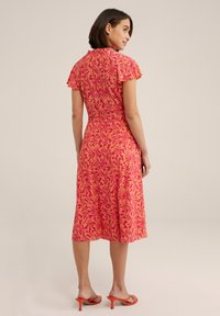 Pink dress with short ruffled sleeves, floral pattern in orange, fitted waist, flowing skirt, and person wearing orange heeled sandals.