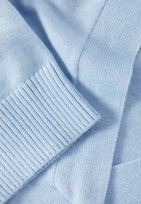 Tissu tricoté bleu clair avec une texture douce. Présente des poignets côtelés et une finition lisse, mettant en valeur des variations subtiles de couleur.