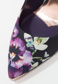Chaussure à bout pointu en tissu sombre avec des motifs floraux violets et blancs ainsi que des papillons, et une doublure intérieure métallique en or rose.