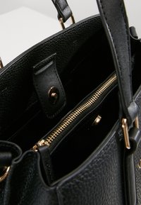 Svart läderhandväska med strukturerad yta, detaljer i guldton och zippered interna fickor för säker förvaring.