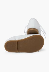 Scarpe bianche in pelle con punta arrotondata, suola piatta in gomma color sabbia e lacci bianchi; cuciture decorative lungo i lati.