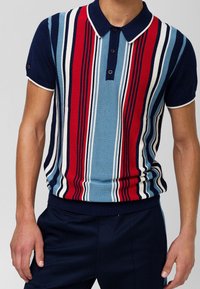 Randig stickad pikétröja med vertikala ränder i röd, blå och vit. Korta ärmar, krage med knappar, ribbad nederkant och mudd.