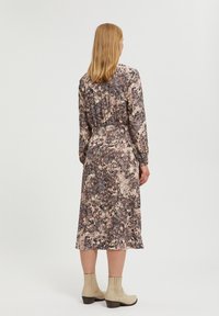 Midiklänning i ett flerfärgat abstrakt mönster med smockad midja och långa ärmar. Bärs med beige ankelstövlar och en texturerad yta.