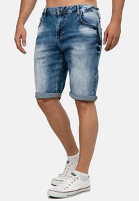 Shorts en denim de lavage bleu clair, avec une coupe décontractée, des ourlets roulés et cinq poches, associés à des baskets blanches.