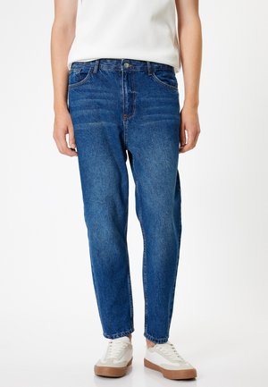 Jeans de mezclilla azul con un ajuste relajado, ligero desgastado, diseño de cinco bolsillos y cierre de botón, combinados con zapatillas color crema.