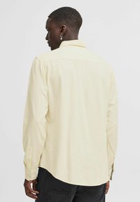 Gul langermet skjorte med klassisk krage, med en glatt tekstur og knappecuff, båret sammen med svarte jeans.