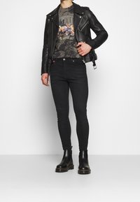 Černá kožená motorkářská bunda přes šedé tričko s grafikou a vzorem tie-dye, spárovaná s černými skinny džíny a černými chelsea botami.