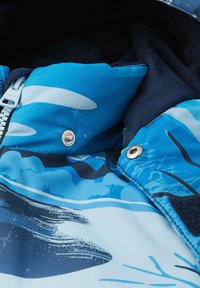 Chaqueta acolchada azul con una tela texturada que presenta patrones abstractos en blanco y azul oscuro. Incluye una cremallera y botones de metal.
