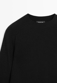 Pull noir à col rond avec manches raglan longues, en tissu fin tricoté, comportant une étiquette Massimo Dutti au niveau de l'encolure.