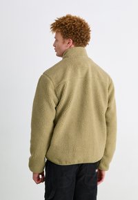 Fleece jacket in light olive green, featuring a high collar, textured exterior, and casual fit. Plain back with no visible logos or accents.