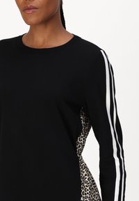 Schwarzes Sweatshirt mit kontrastierenden weißen Streifen an den Ärmeln und einem Leopardenmuster-Panel an der Seite. Weicher Stoff mit rundem Halsausschnitt.