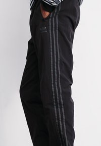 Melnas sporta bikses ar trim vertikālām līnijām un Adidas logo kreisajā kājā. Izgatavotas no gludas, vieglas materiāla.