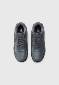 Ζευγάρι σκούρων γκρι και μωβ αθλητικών παπουτσιών Nike με κορδόνια, απεικονιζόμενο από πάνω σε λευκό φόντο.